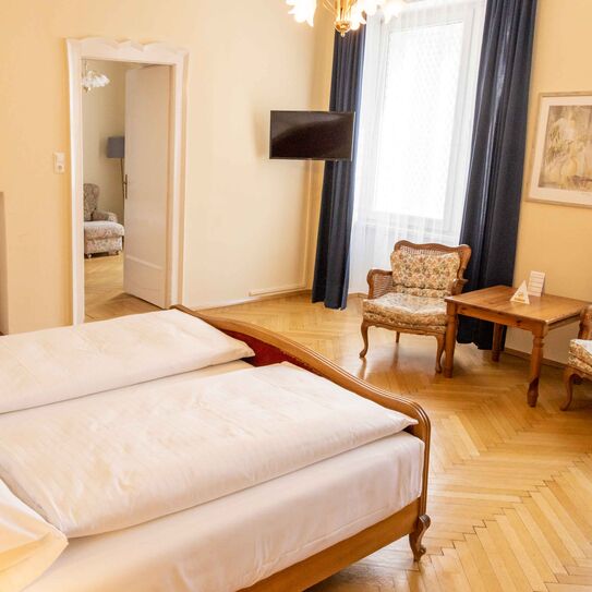 Foto zeigt großzügige Suite mit Blick vom Bett in den Raum mit Mobiliär im Jugendstil.